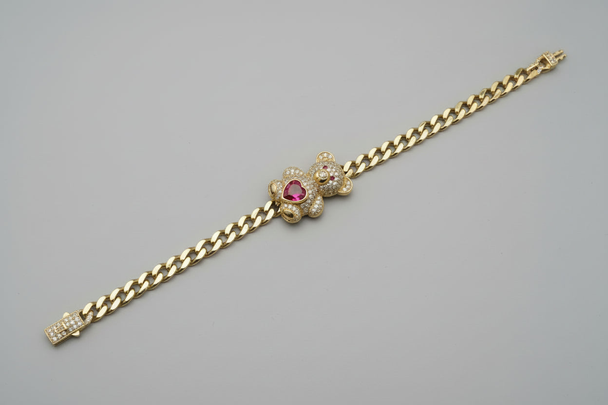 Gold chain bracelet with a bear head charm on a gray surface