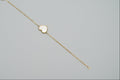 Gold bracelet with a heart-shaped charm on a mannequin arm against a gray background
