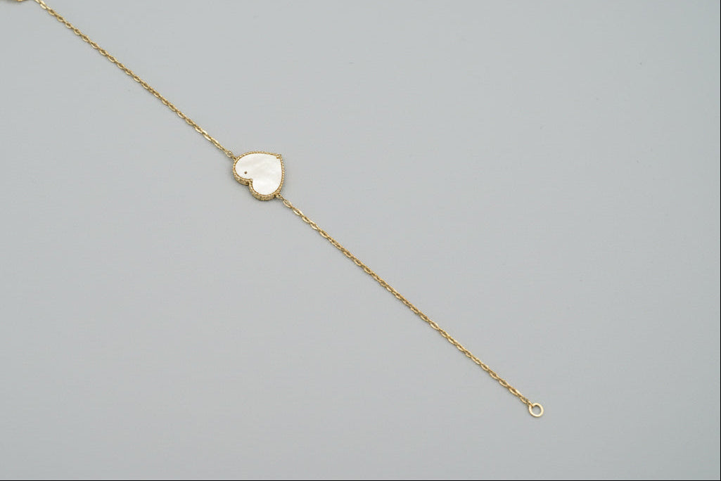 Gold bracelet with a heart-shaped charm on a mannequin arm against a gray background